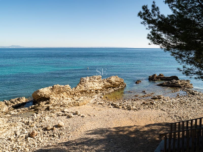 Erhöhte Aussicht auf eine felsige Mittelmeerbucht mit klarem türkisfarbenem Wasser und weitem Horizont.