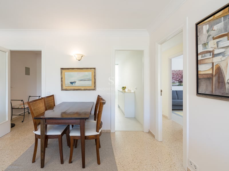 A dark wood dining table and four chairs with woven backs and white cushions in a bright, white room.