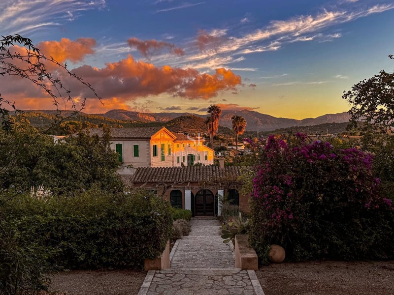 Naturskön utsikt över en vit medelhavsvilla med terrakottatak vid solnedgången, omgiven av prunkande trädgårdar och berg.