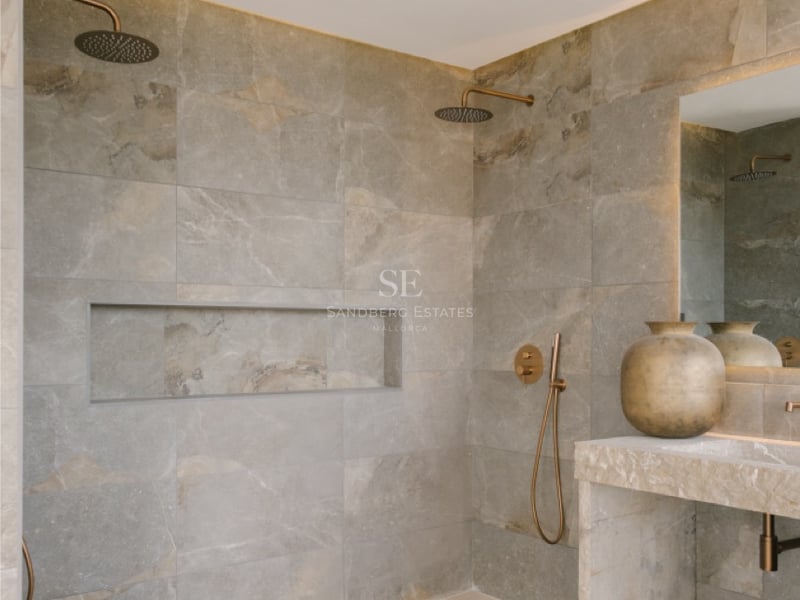 Luxuriöse begehbare Dusche mit großformatigen Natursteinfliesen, Doppel-Regenduschköpfen aus Bronze und Steinwaschtisch.