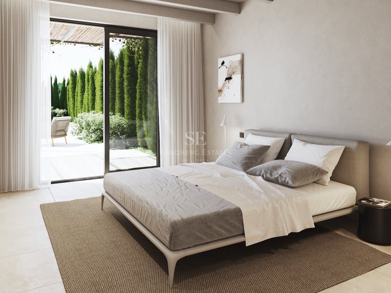 Chambre contemporaine avec poutres en bois, grand lit et baies vitrées ouvrant sur un jardin ensoleillé.