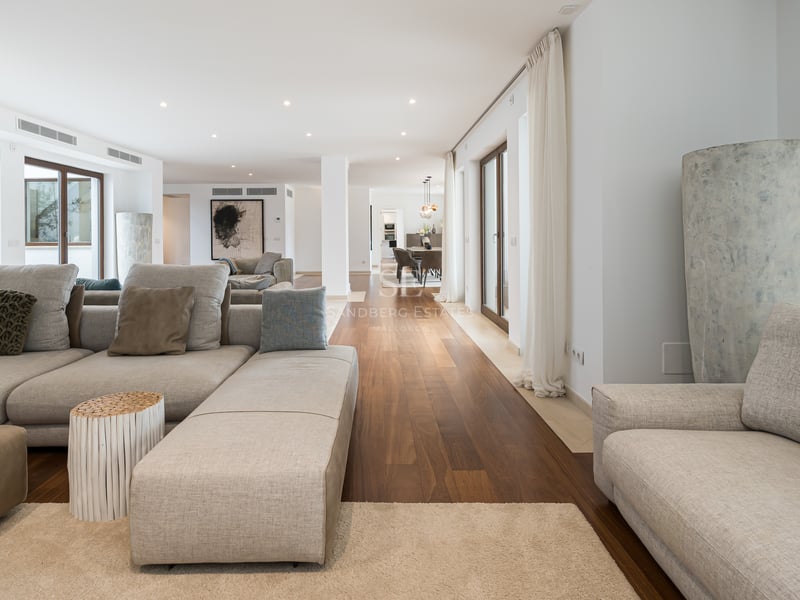 Salon moderne spacieux avec canapés en tissu gris, parquet en bois foncé et baies vitrées.