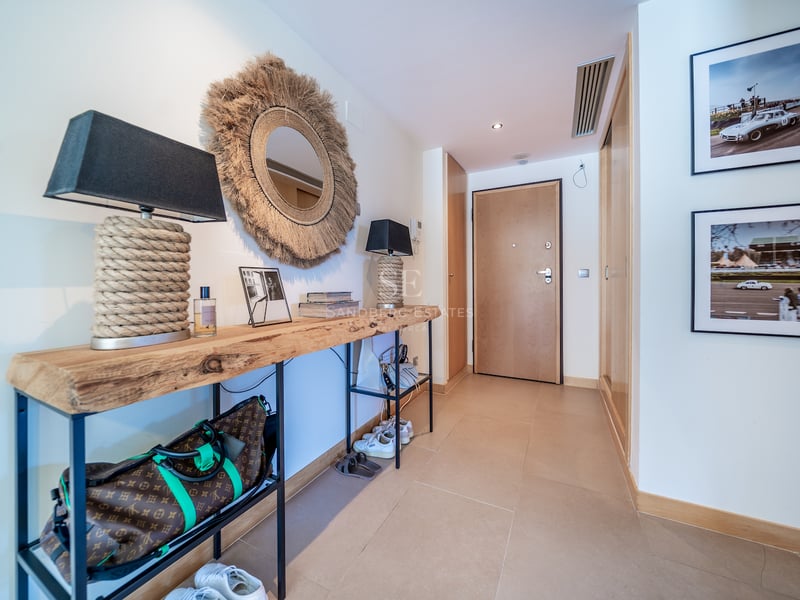 Couloir d'entrée moderne avec console en bois brut, miroir en jute et carrelage beige chaleureux.