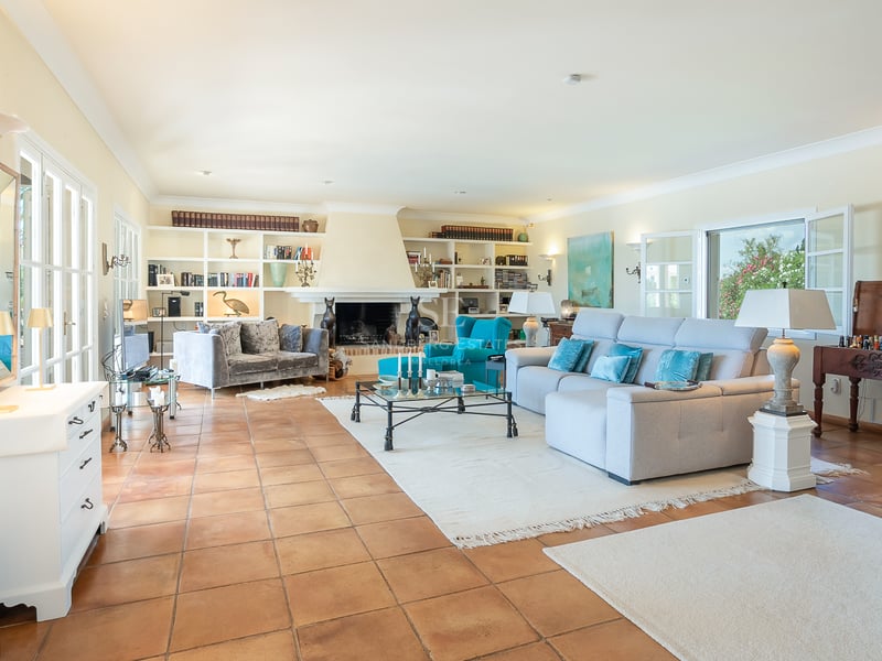 Grand salon avec sol en terre cuite, une grande cheminée blanche et des étagères de bibliothèque intégrées.