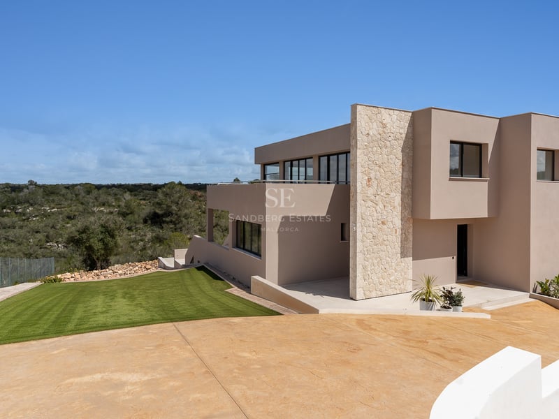 Moderne zweistöckige Villa mit sandfarbener Fassade, Natursteinakzenten und großen Fenstern mit Blick auf den Rasen.