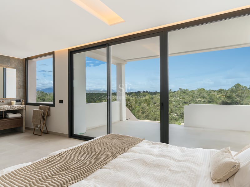 Hauptschlafzimmer mit großen Glasschiebetüren, die auf eine private Terrasse mit Blick auf grüne Hügel führen.