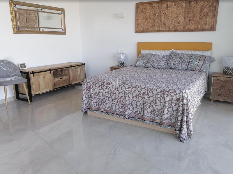 Chambre avec lit double, tête de lit en bois sculpté, sol en marbre poli et lumière naturelle.