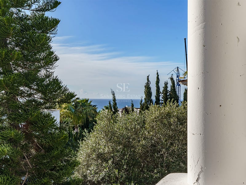 Utsikt över Medelhavet inramad av en vit pelare och frodig grönska under en blå himmel.