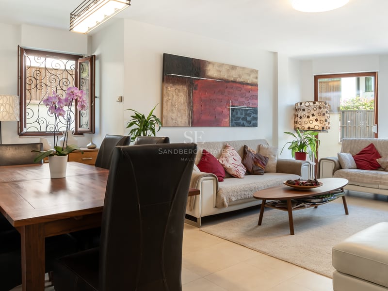 Espace de vie ouvert comprenant des canapés beiges, une table en bois massif et des fenêtres avec grilles en fer forgé.