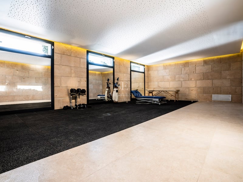 Fitnessraum mit Natursteinwänden, schwarzem Gummiboden, Massageliege und indirekter Deckenbeleuchtung.