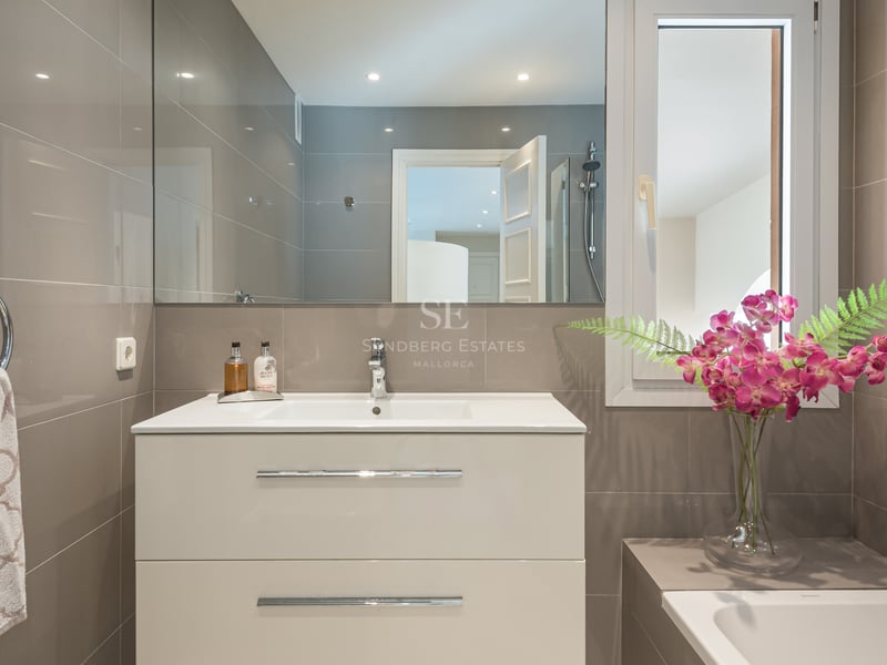 Contemporary bathroom featuring a white vanity, integrated sink, large mirror, and taupe wall tiles with chrome accents.