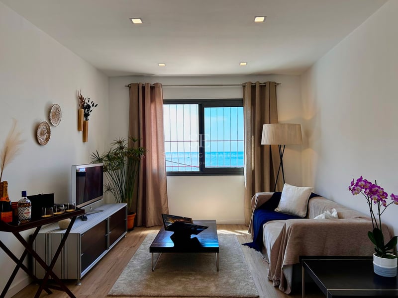 Modern living room featuring a beige sofa, wooden coffee table, and a large window overlooking the blue ocean.