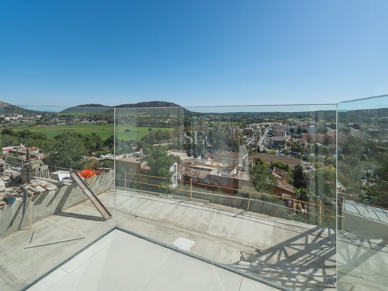 Terrasse moderne en construction avec garde-corps en verre surplombant un village méditerranéen et des collines.