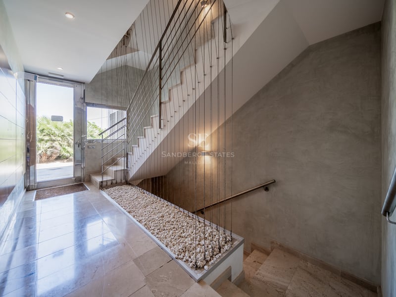 Entrée lumineuse avec sol en pierre polie, escalier à câbles et porte vitrée donnant sur le jardin.