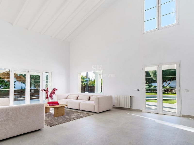 Rymligt vardagsrum med vita ryggåstak, beige soffor och altandörrar som leder ut till trädgården.