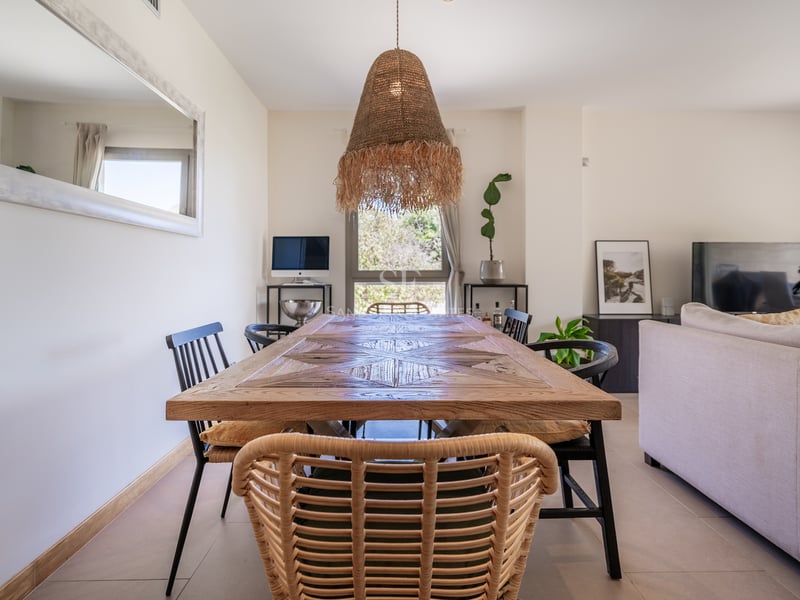 Grande table à manger en marqueterie de bois avec suspension en rotin dans un salon moderne et lumineux.