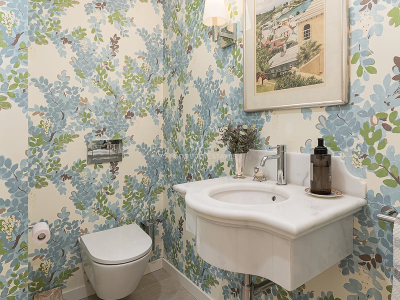 Guest bathroom featuring floral wallpaper, a sculpted marble washbasin, and a wall-mounted toilet.