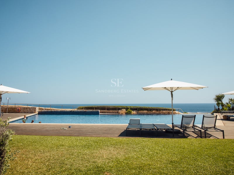 Grande piscine extérieure avec terrasse en bois et chaises longues face à la mer sous un ciel bleu.