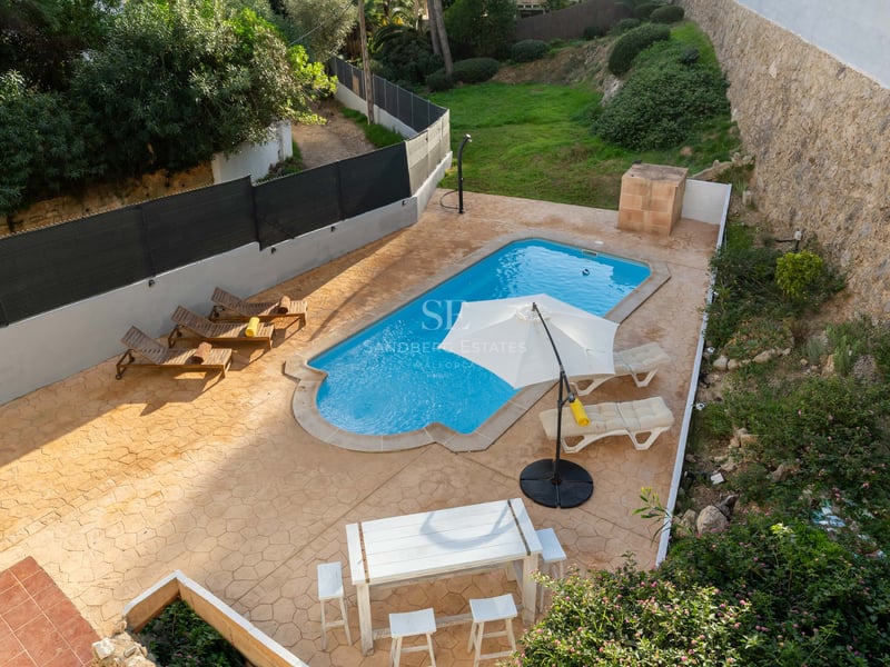 Vue aérienne d'une piscine turquoise entourée d'une terrasse en terre cuite avec transats et coin repas.