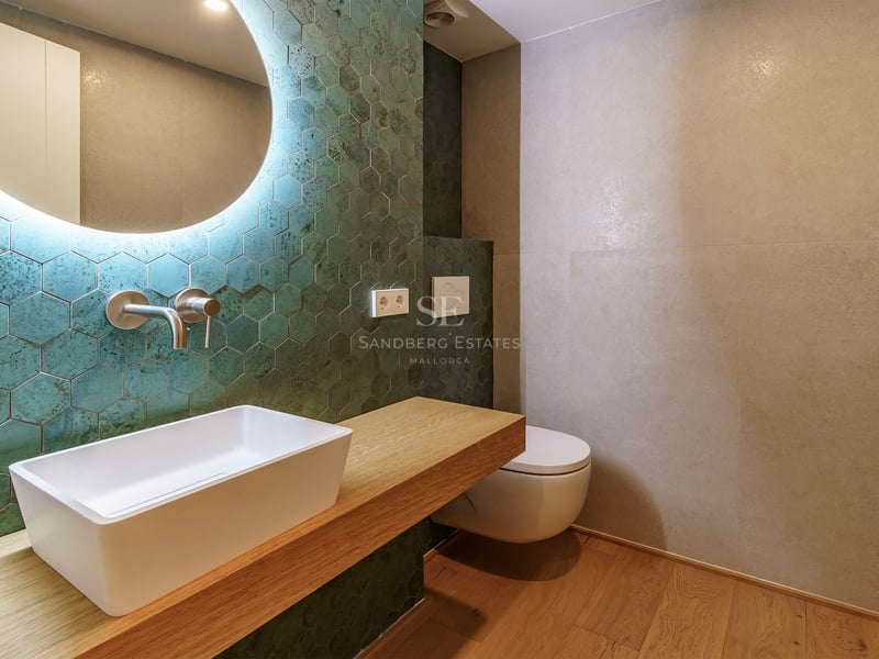 Salle de bain moderne avec carreaux hexagonaux vert canard, vasque à poser sur bois et miroir rétroéclairé.