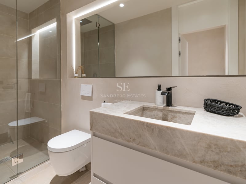 Salle de bains moderne avec vasque en marbre, miroir rétroéclairé, WC suspendu et douche à l'italienne en verre.