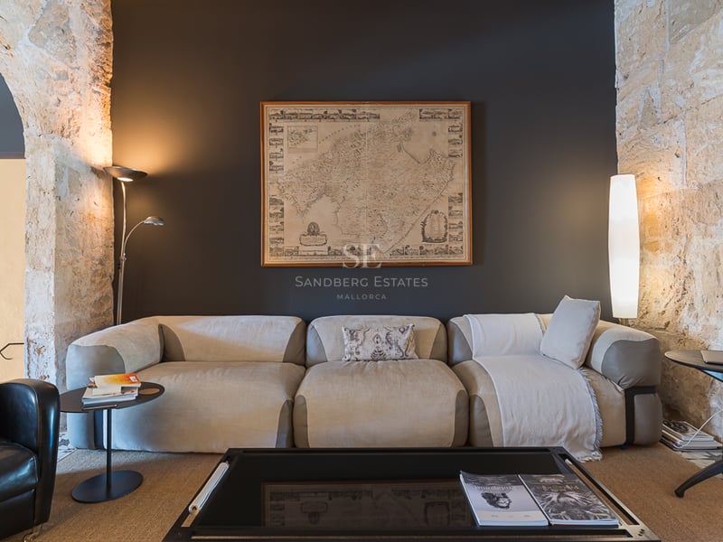 Canapé beige moderne devant un mur anthracite avec carte de Majorque et arches en pierre apparente.