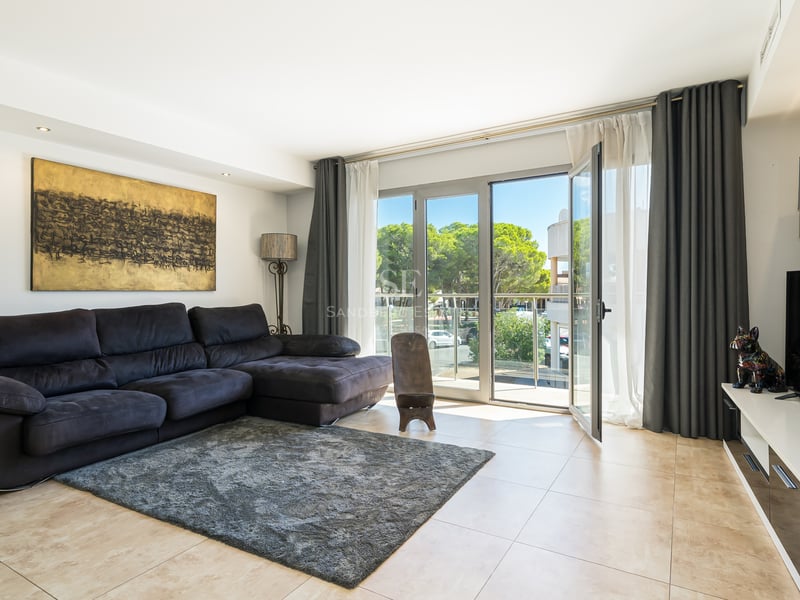 Ljust vardagsrum med en stor mörk soffa, grå matta och stora fönsterpartier som leder ut till en balkong.