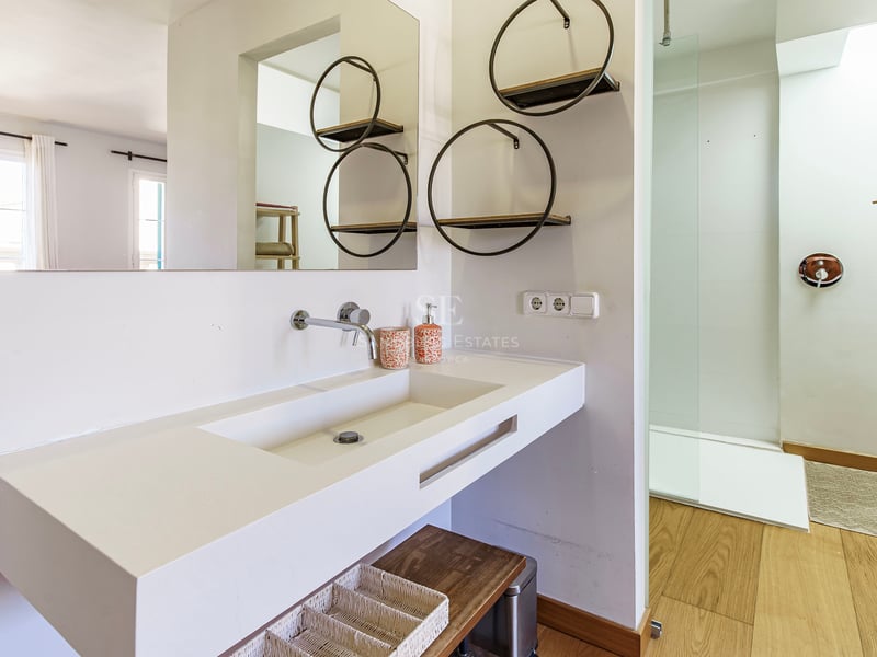 Modernt vitt badrum med stort integrerat handfat, runda vägghyllor och en duschkabin i glas.