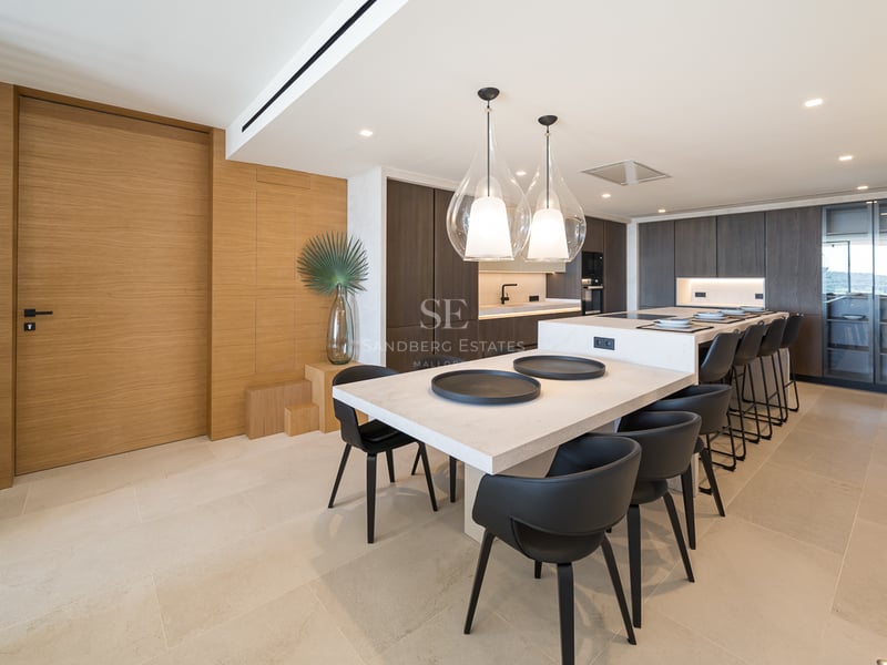 Cuisine moderne à aire ouverte avec îlot en pierre, armoires en bois sombre et suspensions design.