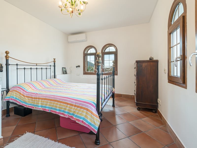 Bright bedroom featuring terracotta tile flooring, a wrought iron bed frame, and traditional arched wooden windows.