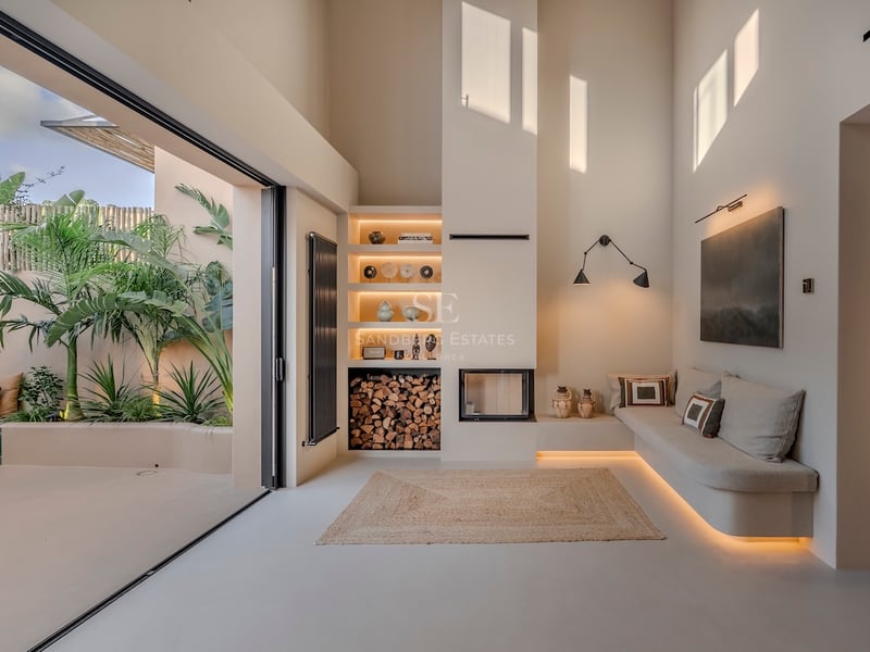 Salon épuré avec cheminée intégrée, banquette sur mesure et grandes baies vitrées donnant sur un jardin tropical.