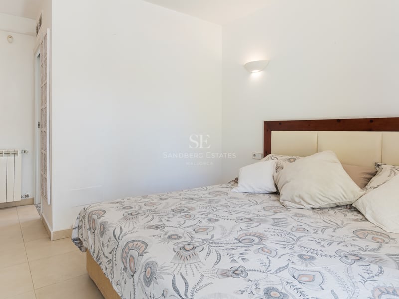 Chambre avec literie à motifs, murs blancs, carrelage crème et tête de lit en bois avec appliques murales.