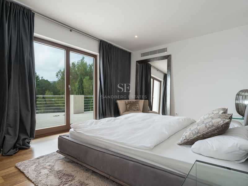 Chambre principale contemporaine avec literie blanche, rideaux anthracite et baies vitrées ouvrant sur une terrasse.