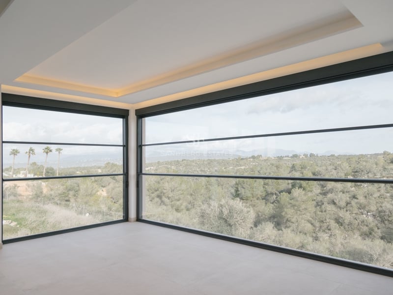 Moderner leerer Raum mit bodentiefen Eckfenstern und Blick auf eine üppige grüne Landschaft und ferne Berge.