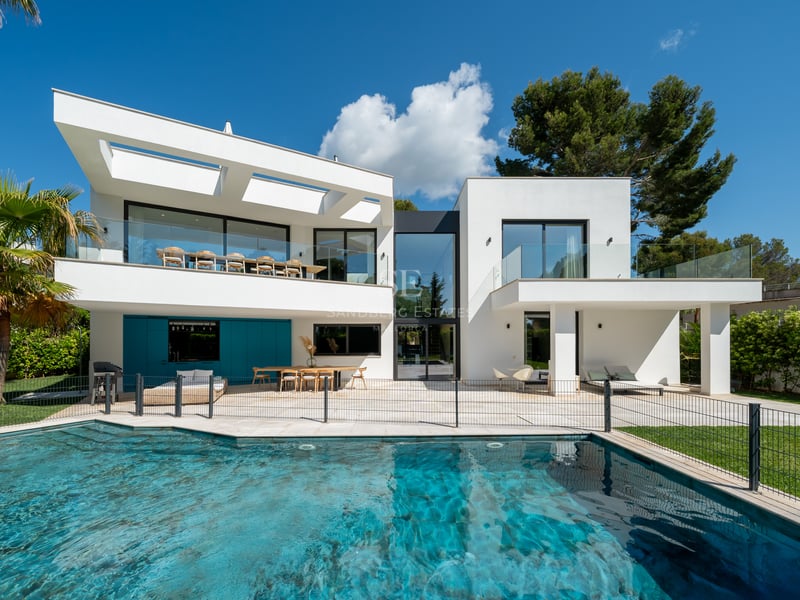Extérieur d'une villa blanche moderne avec grande piscine, balustrades en verre et palmiers.