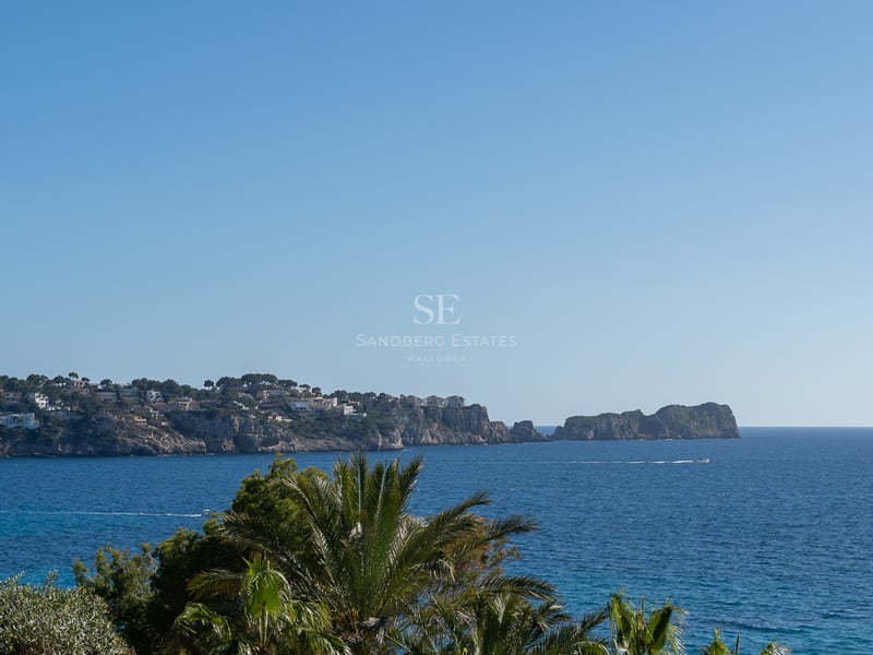 Weitwinkelblick auf das Mittelmeer mit Klippen, Luxusvillen und Palmen unter einem klaren blauen Himmel.