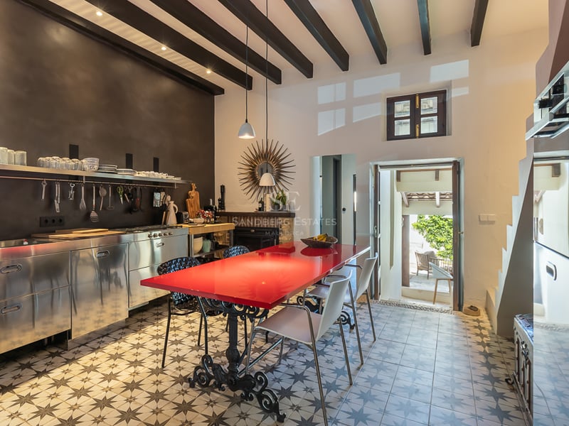 Cuisine moderne avec placards en inox, table rouge et carrelage hydraulique traditionnel.