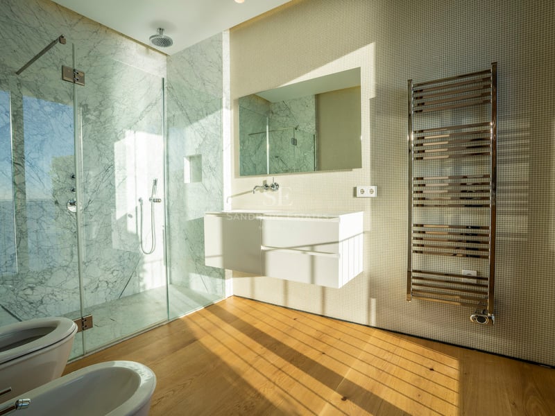 Modernes Badezimmer mit bodengleicher Marmordusche, schwebendem Waschtisch und Eichenparkett im Sonnenlicht.