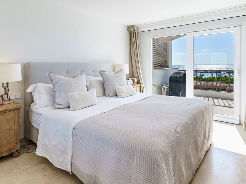 Bright bedroom featuring a large bed, wooden nightstands, and sliding glass doors with views of the sea and marina.
