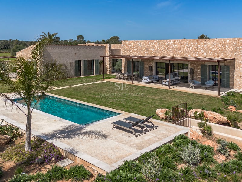 Außenansicht einer Steinvilla mit rechteckigem Pool, Rasenfläche und Pergola-Terrasse in Mallorca.