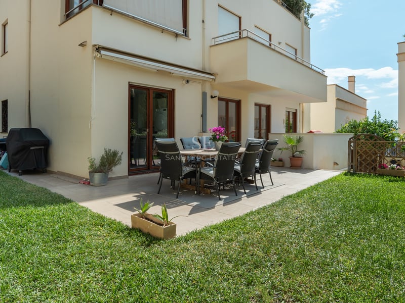 Patio extérieur avec table à manger et chaises sur une terrasse carrelée entourée d'une pelouse verte soignée.