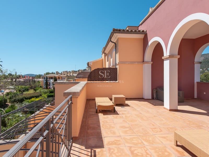 Sunny terracotta terrace with arches, sun loungers, and views of lush gardens and hills under a clear blue sky.