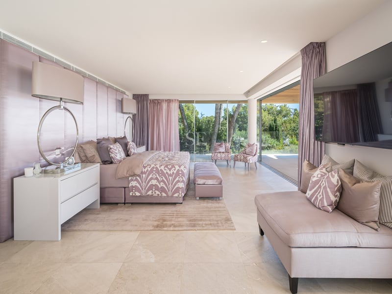 Luxuriöses Schlafzimmer mit Kingsize-Bett und Glasfronten zum grünen Garten.