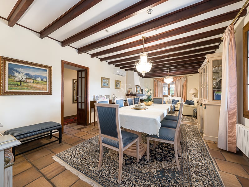 Salle à manger formelle avec poutres en bois sombre, sol en terre cuite et grande table sous un lustre classique.