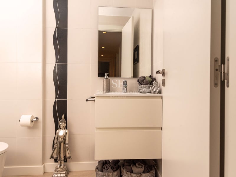 Cremefarbenes Badezimmer mit weißem Waschtisch, rechteckigem Spiegel und silberner Buddha-Statue.