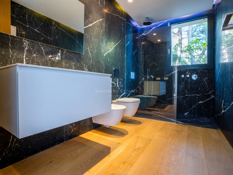 Modernes Bad mit schwarzen Marmorwänden, Eichenboden, weißem Waschtisch und verglaster Dusche.