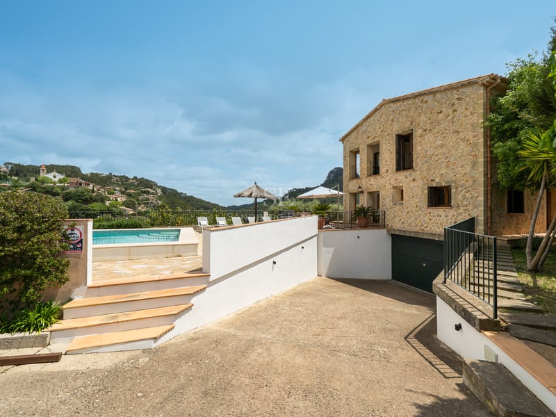 Vue extérieure d'une villa en pierre avec piscine, terrasse ensoleillée et vue sur la montagne par temps clair.