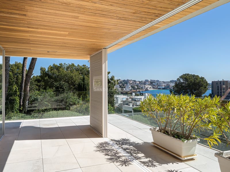 Moderne Terrasse mit hochwertiger Holzdecke, Glasgeländer und weitem Blick auf die Küstenbucht.