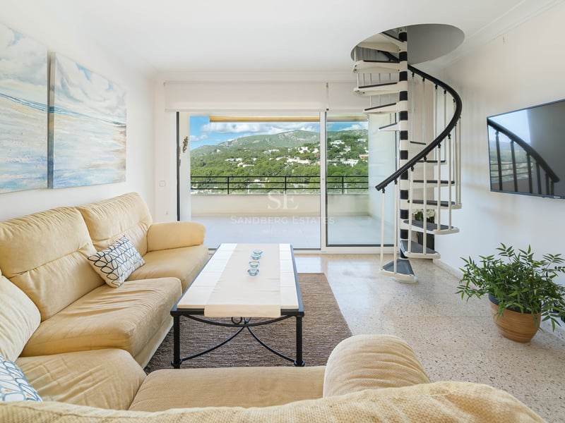 Bright living room featuring a cream sofa, black and white spiral staircase, and balcony with mountain views.