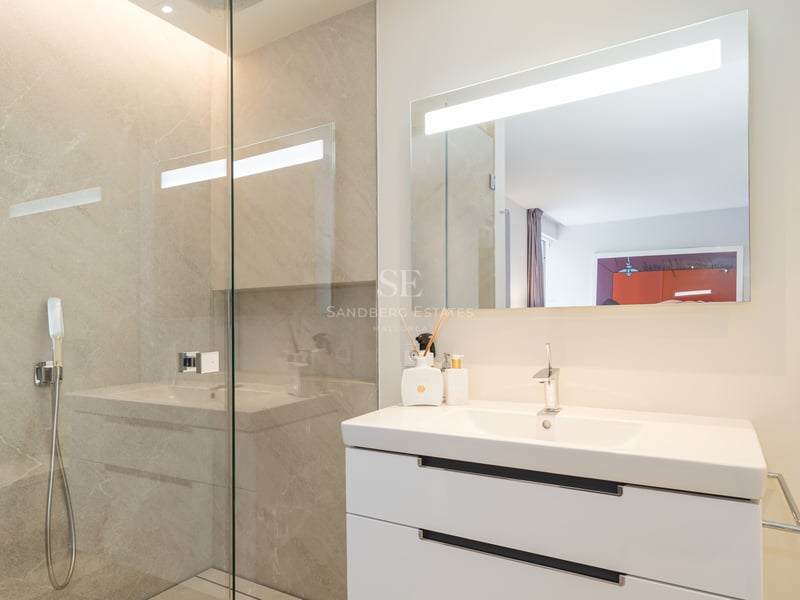 Modernes Badezimmer mit weißem Waschtisch, großem LED-Spiegel und rahmenloser Glasduschwand.